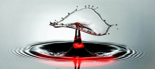 A drop falling and splashing into a pool of red liquid which splashes up.