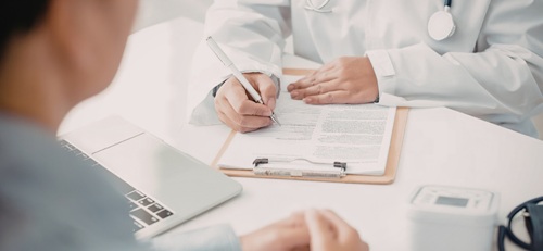 Close up view of two women, their hands o the desk, one with a clipboard in what appears to be a medical appointment or discussion