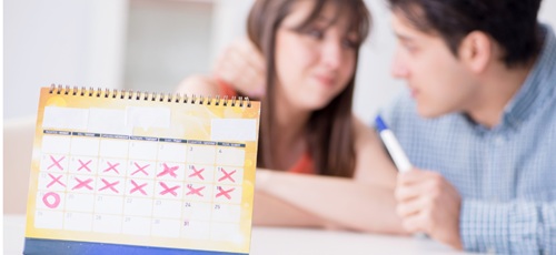 Couple in background with pregnancy test, in the front a calendar with date for ovulation circled