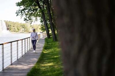 A woman walking in a park alongside a river.