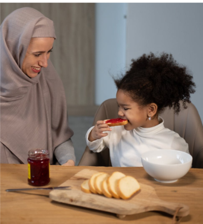  Picture of a young girl eating jam on bread, with her mother.