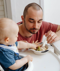 Picture of a father feeding his baby in a highchair.