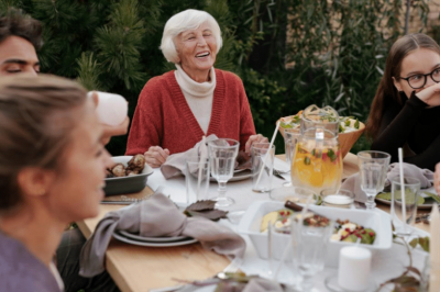 A photo of an older woman enjoying a lunch outside with a group of people.