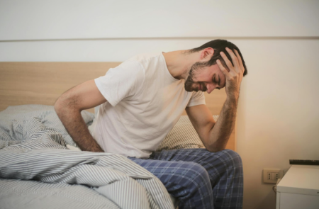 A photo of a man in discomfort, sat on the edge of the bed