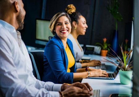 A photo of three people talking happily at a desk with laptops