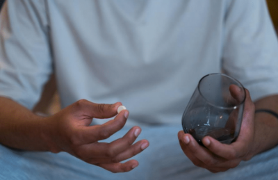 A person holding a pill and a water glass.